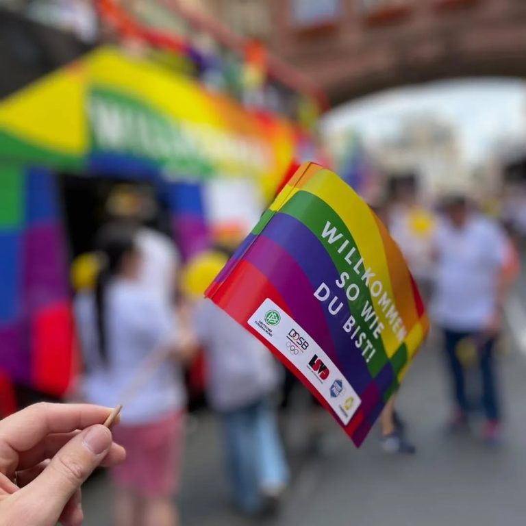 Hand hält SportPride-Papierfähnchen